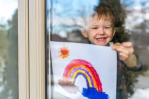child holding up picture of rainbow to window
