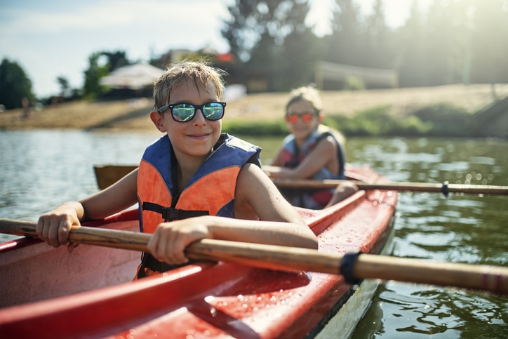 Two boys enjoying kayaking on lake on sunny summer day.