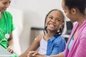 Cheerful African American elementary age girl receives an immunization from a nurse. The girl is sitting next to her mother.